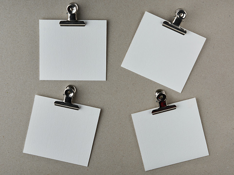 white blank paper notes with metal clips, isolated on gray textured board surface, note or messages template, taken straight from above