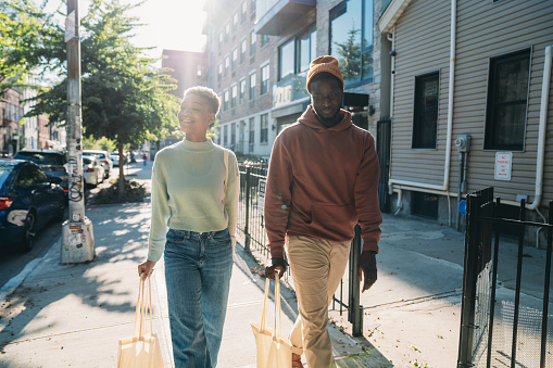 A couple is walking on the street in Bushwick, Brooklyn, New York City. They are holding cotton shopping bags.