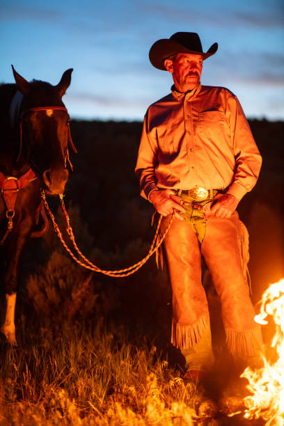 istock Cowboy Standing With Horse In Front Of Campfire - Vertical 1434483159