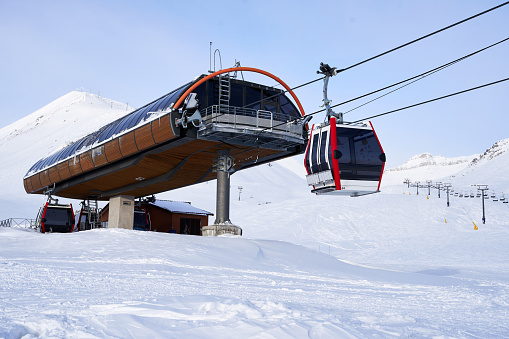 Cable car gondola at ski resort with snowy mountains on background. Modern ski lift with funitels and supporting towers high in the mountains on winter day. A ski lift station with no people.