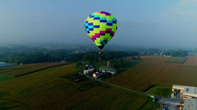 Drone View of a Single Hot Air Balloon Floating By Over Farms and Businesses