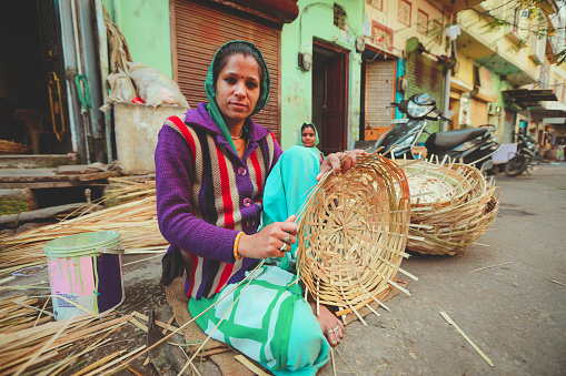 Jaisalmer, India - January 19, 2020 : Soft focus on Indian woman weaves a bamboo basket . Bamboo basketry made vase.