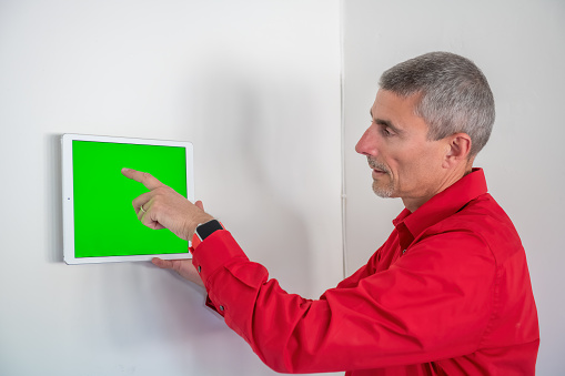 Smart home and technology concept, male hands pointing finger to a tablet with green screen integrated in house indoor wall