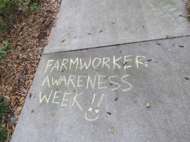 White Chalk words on cement walkway Farmworkers Awareness Week with happy face.
