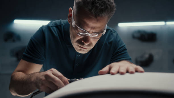 Experienced car designer with safety goggles uses a rotary tool for cutting edge Experienced car designer works closely on the prototype car model in a high tech car manufacturing company. Wearing safety goggles using a handheld rotary tool for cutting edge. industrial designer stock pictures, royalty-free photos & images