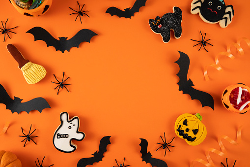Halloween decorations, pumpkins, bats, ghosts, cookies and candies on orange background with copy space