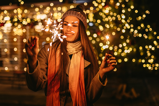 Young woman in front of a café, holding sparkles, celebrating Christmas.
