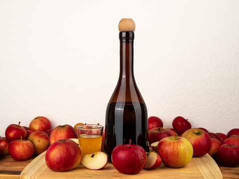 Apple cider vinegar in a bottle with apples against a white wall. Apple cider vinegar and apples.