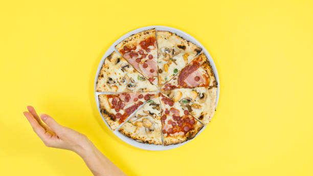 istock Woman's hand near pizza on white plate. Yellow background. 1434511283