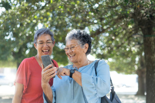 Happy senior friends looking at phone outside stock photo