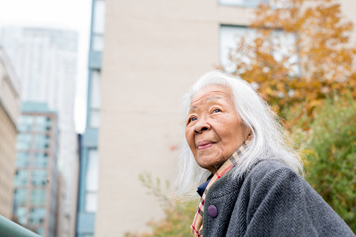 Portrait of a senior Filipino woman standing on a rooftop patio overlooking downtown Toronto on an autumn day