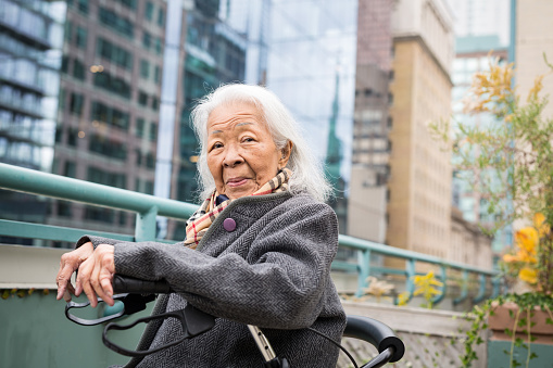 Portrait of a Filipino woman sitting in her mobility walker on a rooftop patio overlooking downtown Toronto on an autumn day
