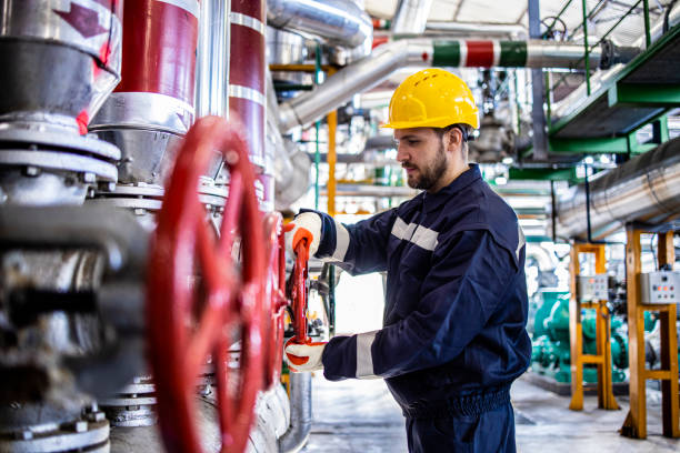 Industrial worker in safety work wear and hardhat working in refinery controlling gas production. Factory interior and pipeline in background. stock photo