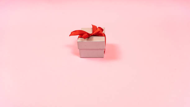 istock Small gray gift box tied with a red ribbon with a present for a loved one isolated light pink pastel background. Copy space 1434513745