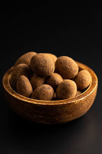 Almonds in chocolate coated in cocoa in bowl on a dark table.