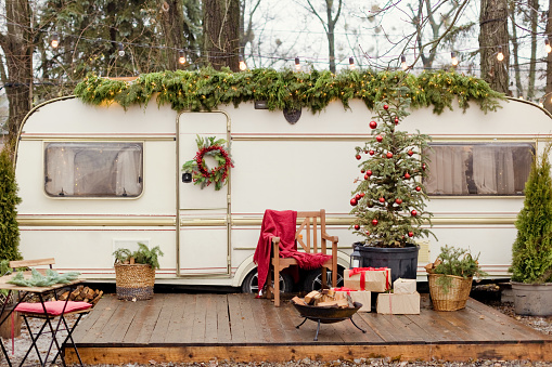 Vintage old travel trailer with Christmas decorations, Christmas tree, chair and Christmas lights. Cozy home, camping before Christmas holidays.