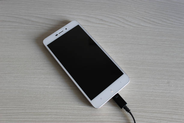 istock Mobile Phone With Screen Off On A Wooden Shelf Connected By Cable For Data Transfer And Charging Top View 1434515953