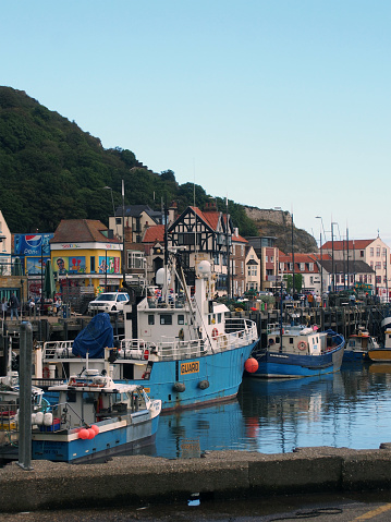 Scarborough, North Yorkshire, United Kingdom - 11 September 2022: fishing boats and a trawler in the harbour in Scarborough with shops and tourists along the seafront