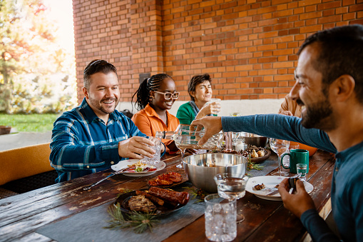 Diverse mid adult Friends sharing and enjoying meal together at dining table