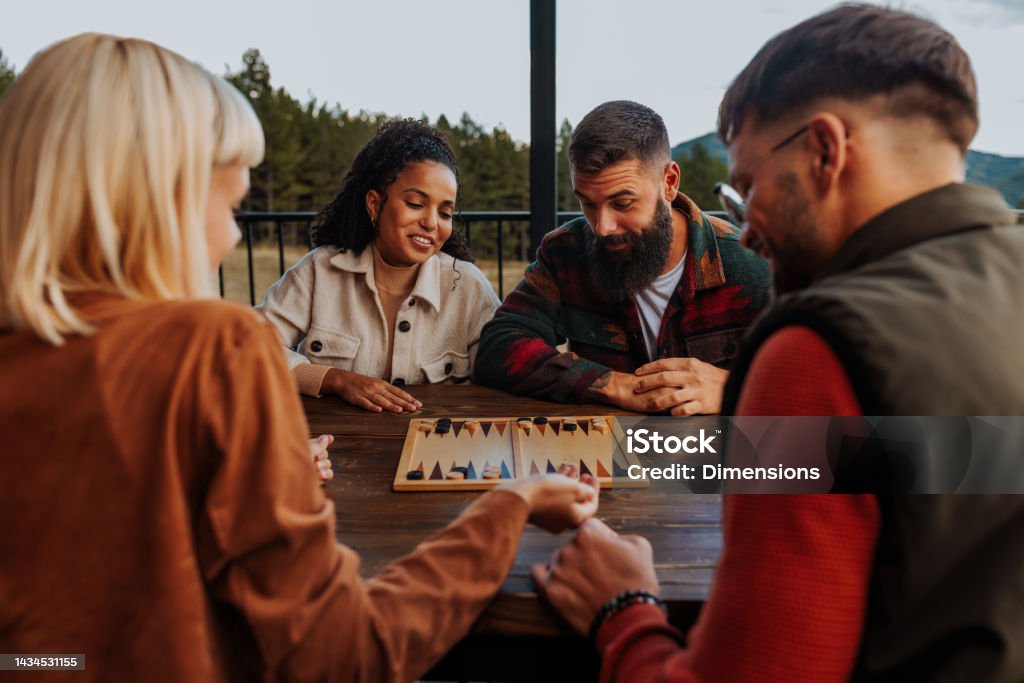 Friends playing backgammon on mountain. A couple of young friends are playing a game of backgammon outdoors on their mountain weekend getaway. Board Game Stock Photo