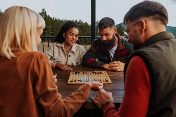 A couple of young friends are playing a game of backgammon outdoors on their mountain weekend getaway.