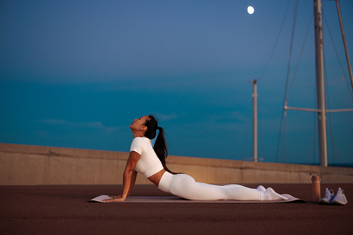 A young woman is outdoors in the city urban area stretching on a yoga mat.