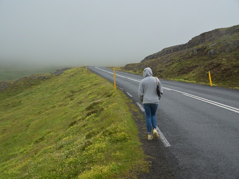 A person walking alongside a highway near hills on a foggy day