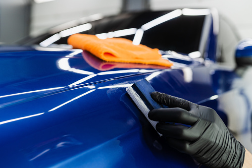 Process of applying ceramic protective coat on body car using sponge in detailing auto service. Car service worker apply ceramic coating to protect the car body from scratches.