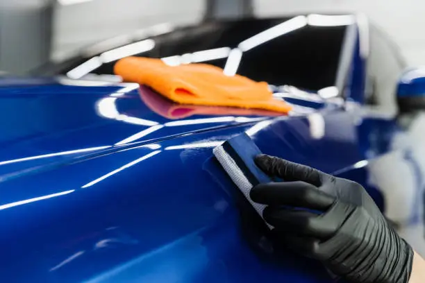 Photo of Process of applying ceramic protective coat on body car using sponge in detailing auto service. Car service worker apply ceramic coating to protect the car body from scratches.