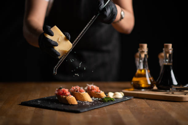 uma chef fêmea ralada queijo em bruschetta - bread cheese bruschetta canape - fotografias e filmes do acervo