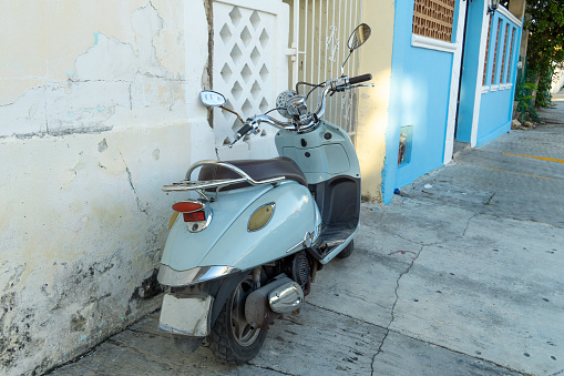 A small blue scooter is parked in front of a colonial building. Lonely motorcycle on the street of a resort town, Mexico.