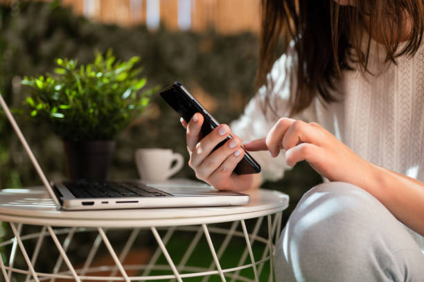 istock Close up of women's hands holding mobile phone while working online on laptop and drinking coffee. 1434548664