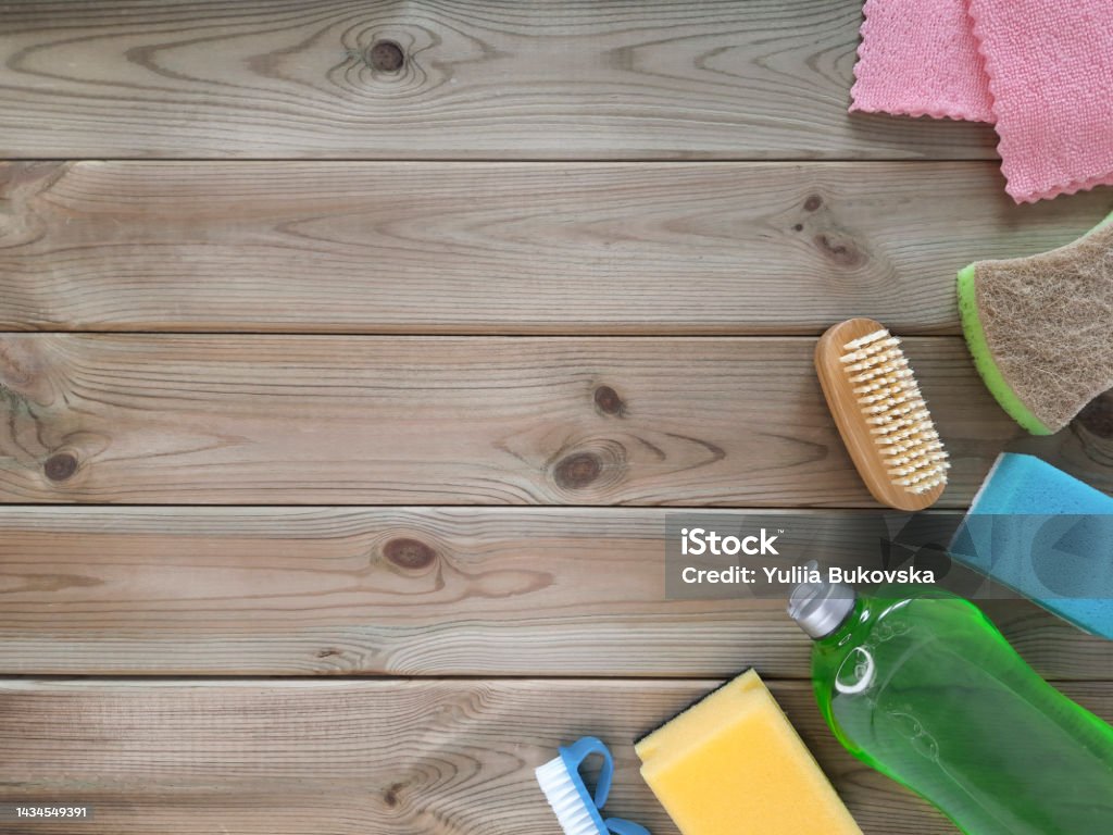 Accessories for cleaning at right on wooden light background. Cleaning service concept. Flatlay. Mockup for advertisement with copy space Dishwashing liquid, brushes and washcloths lie on one side on boards. Top view. Cleaning Product Stock Photo