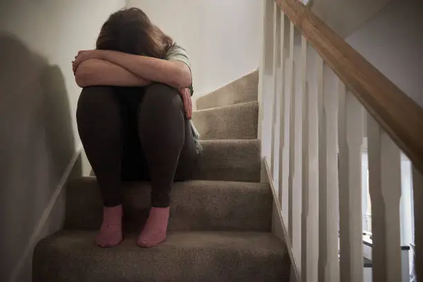 A woman suffering from depression or domestic abuse sat on the stairs of her home hiding her face.