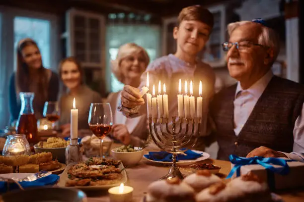 Close up of kid and his extended family lighting the menorah during dinner at dinning table on Hanukkah.