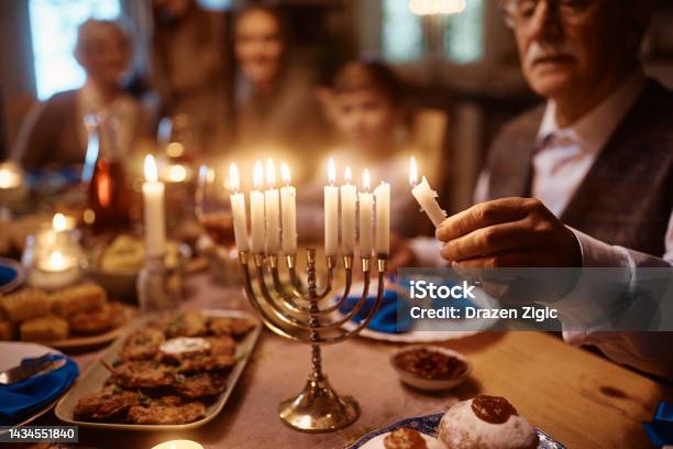 Close Up Of Senior Man Lighting Menorah During Family Dinner On Hanukkah Stock Photo - Download Image Now