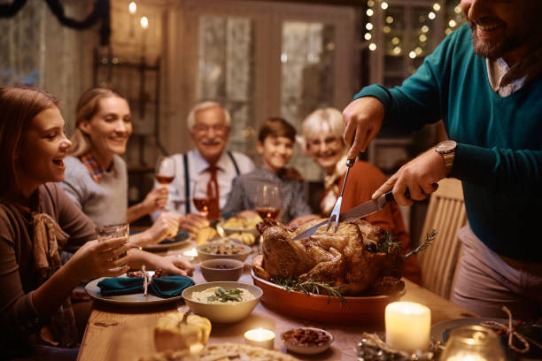 zbliżenie na mężczyznę rzeźbiącego mięso z indyka podczas posiłku w święto dziękczynienia ze swoją dalszą rodziną. - roast turkey turkey cutting roasted zdjęcia i obrazy z banku zdjęć