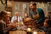 Happy father serving Thanksgiving turkey to his extended family at dining table.