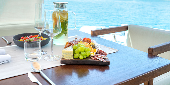 Served portions on tasty lunch on yacht. Sliced sausages, mould cheese and fresh fruit and vegetable. Luxury vacation at sea.