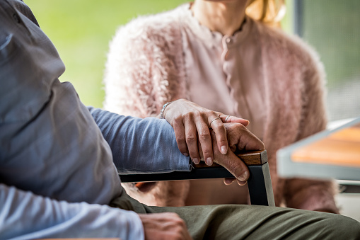 Senior man and woman holding hands closeup, sitting in garden. Female caregiver supporting grandfather, couple assistance and  caregiving concept