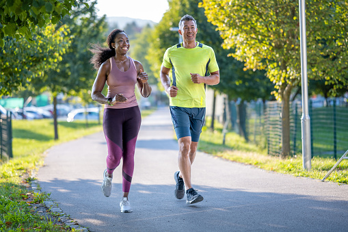 Young man and woman jogging in urban area together, wide shot. Two people running in city, long angle front view