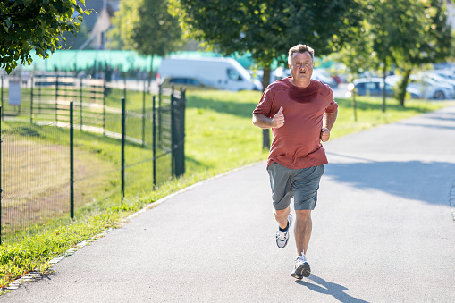 Healthy lifestyle, mid adult man jogging in road, wide shot. Person in sportswear running in street, doing sports outdoors, front view