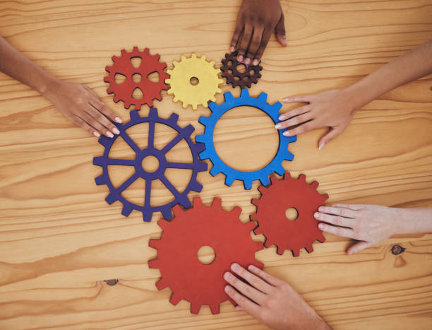 istock Hands, gears and collaboration with a team of people working with cogs and equipment on a table in the office. Teamwork, synergy and planning with a business group meeting to talk company strategy 1434577763