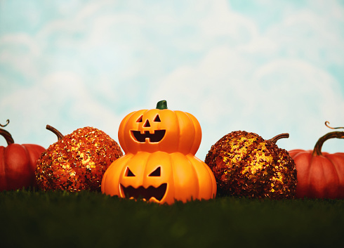 Jack O'lanterns with pumpkins in grass with cloudy sky. Space for text