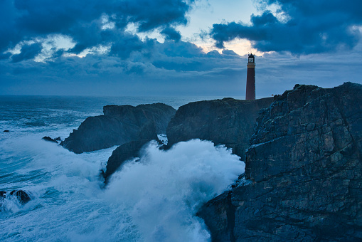 Lighthouse on cliff edge in moody weather and heavy seas
