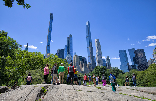 People on a hill enjoying the view of Midtown Manhattan skyline in Central Park.