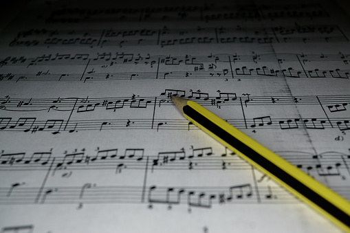 sheet music with blurred black background and a yellow pencil on top of it