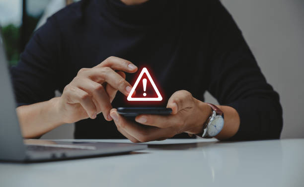 Businessman using smartphone with warning sign. stock photo