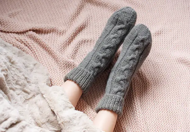 Legs of a young girl in cozy knitted socks. Female legs in warm socks on plaid. Concept of heating season
