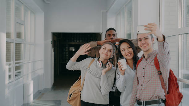 istock Group of multi-ethnic students taking selfie on smartphone camera while standing in corridor of university . Hipster guy holding phone and friends are posing positively 1434615463
